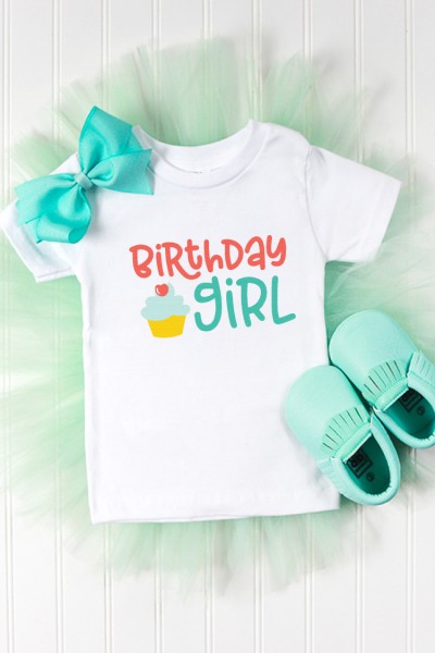 Little aqua colored moccasins, an aqua colored hair bow, and a white t-shirt decorated with an image of a cupcake and the text, "Birthday Girl"