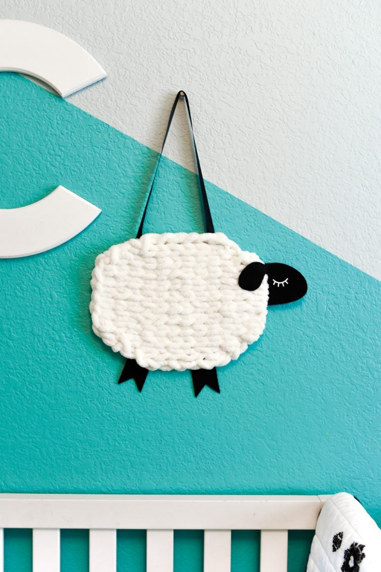 The letter \"C\" and A yarn and felt sheep hanging on a wall above a baby crib