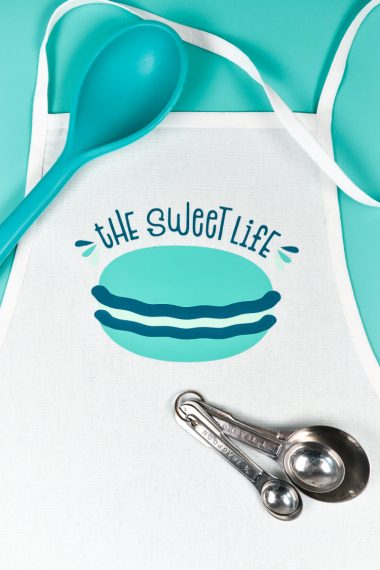 Measuring spoons, large mixing spoon and an apron with the saying, "The Sweet Life" and an image of a macaron