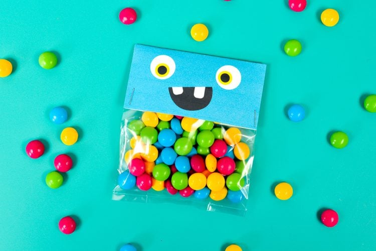 Colorful pieces of candy around a cellophaned bag of the same kind of candy that is decorated with a monster face