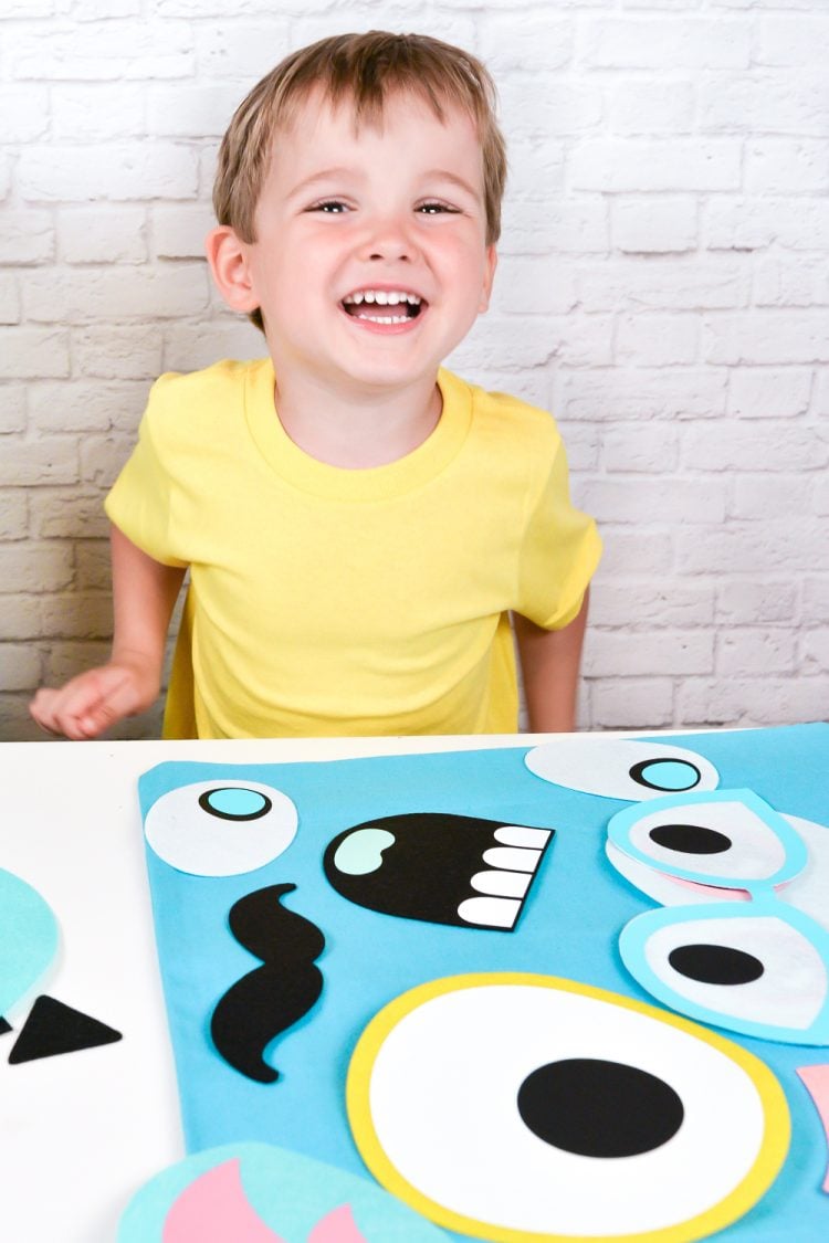 Little boy sitting by a table that has monster shaped face pieces on top of a bag