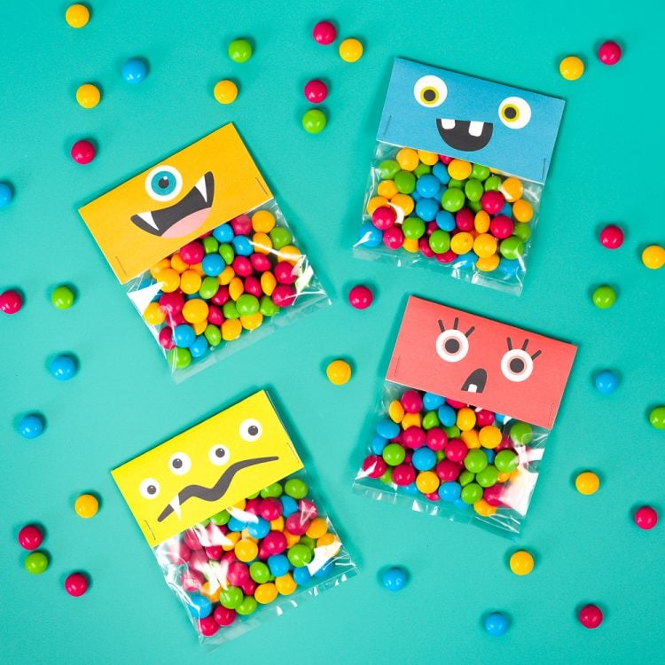 Colorful pieces of candy around several cellophaned bags of the same kind of candy and all are decorated with a monster face
