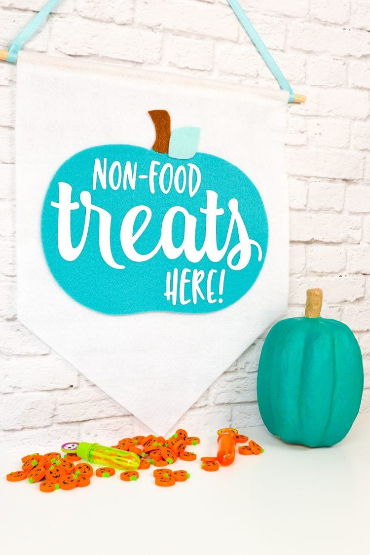 Close up of a teal pumpkin next to a hanging banner that says, \"Non-Food Treats Hear!\"