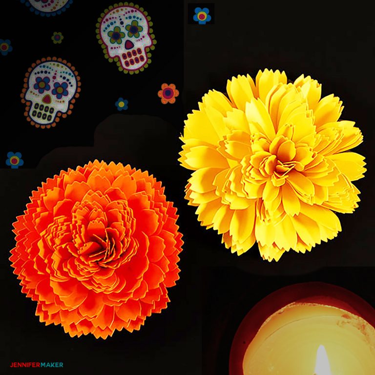 Paper marigold flowers in orange and yellow next to a candle and Day of the Dead decor