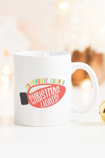 A coffee mug on a table, with and image of a Christmas light with the saying, "My Favorite Color is Christmas Lights!"