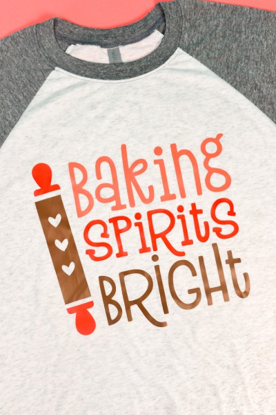 Baseball style shirt with gray sleeves and white body that has an image of a rolling pin and saying, "Baking Spirits Bright"