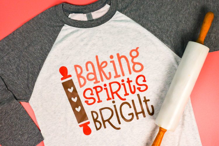 A rolling pin and a baseball style shirt with gray sleeves and white body that has an image of a rolling pin and saying, \"Baking Spirits Bright\"