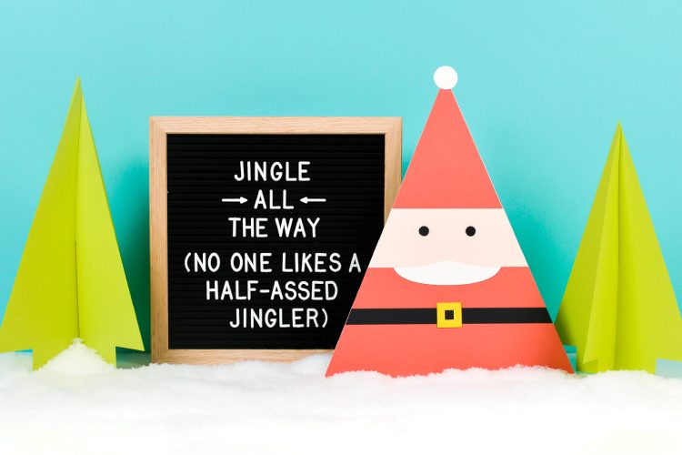 An Image of a Santa and some trees cut from paper and a framed wooden board that says, \"Jingle All the Way (No One Likes a Half-assed Jingler)\"