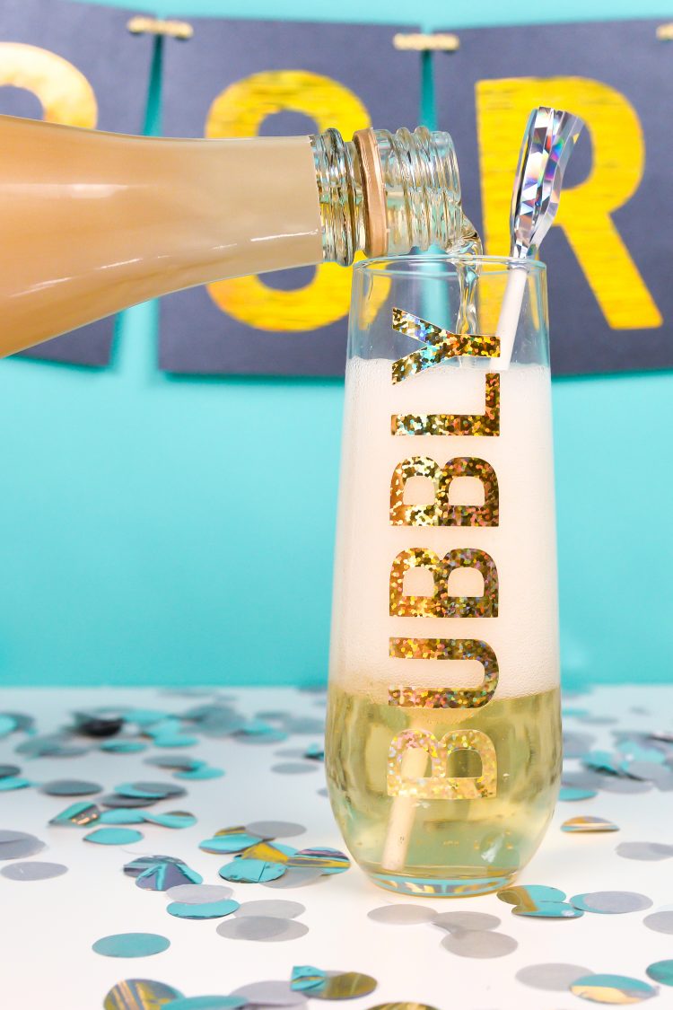Champagne being poured into a glass that is designed with the word \"Bubbly\" on it