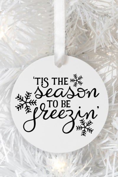 "'Tis the Season to be freezing" image on a round white ornament hanging on a white Christmas Tree