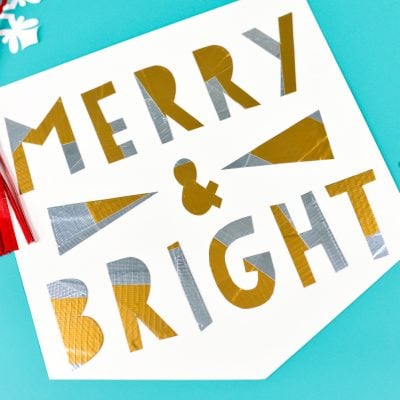 White paper cut snowflakes next to a red Tassel hanging over a sign that says, "Merry & Bright"