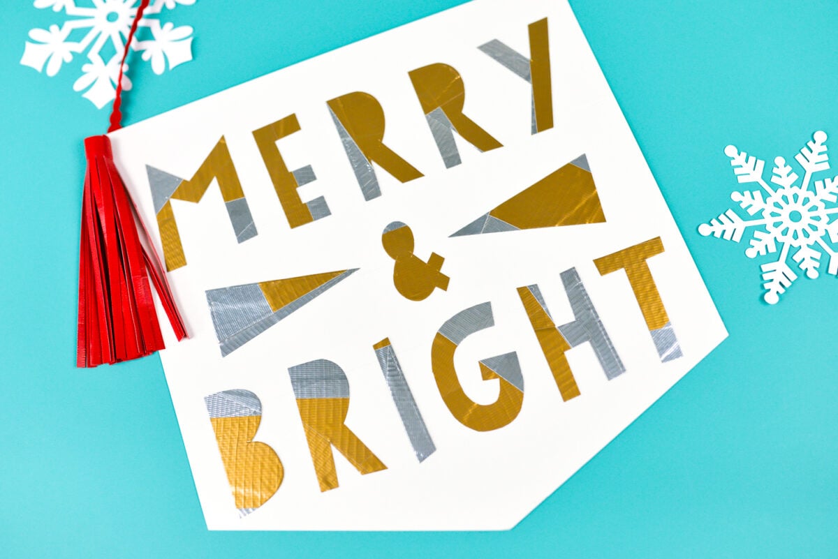 White paper cut snowflakes next to a red Tassel hanging over a sign that says, \"Merry & Bright\"