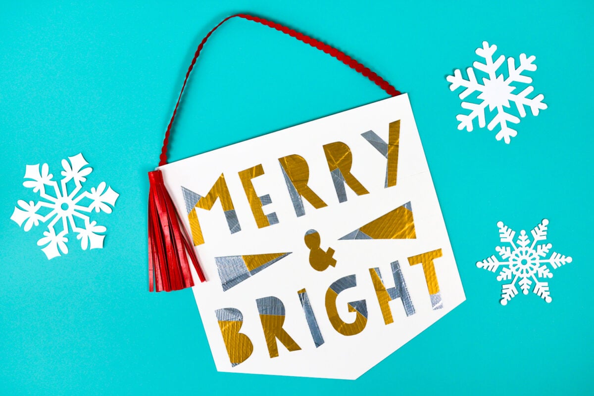 White paper cut snowflakes next to a red Tassel hanging over a sign that says, \"Merry & Bright\"