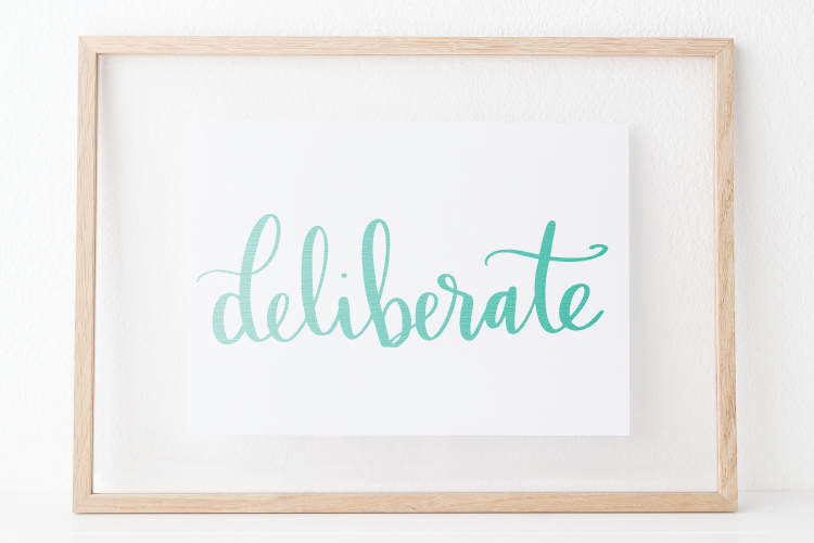 The word \"Deliberate\" on a piece of white paper and framed with a wooden frame