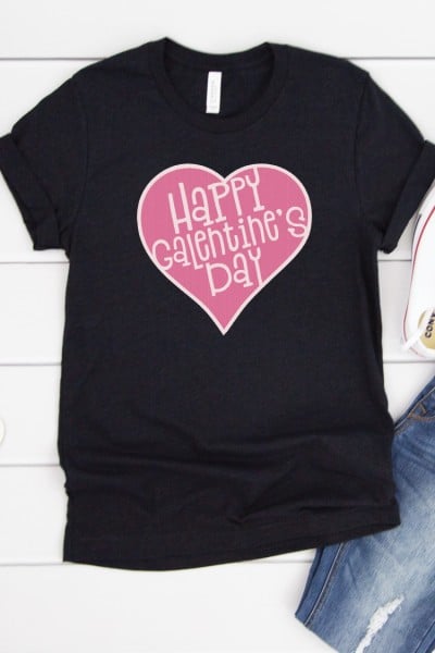 Partial image of a pair of blue jeans and tennis shoes along with a full image of a black t-shirt with a pink heart design and the saying, "Happy Galentine's Day"