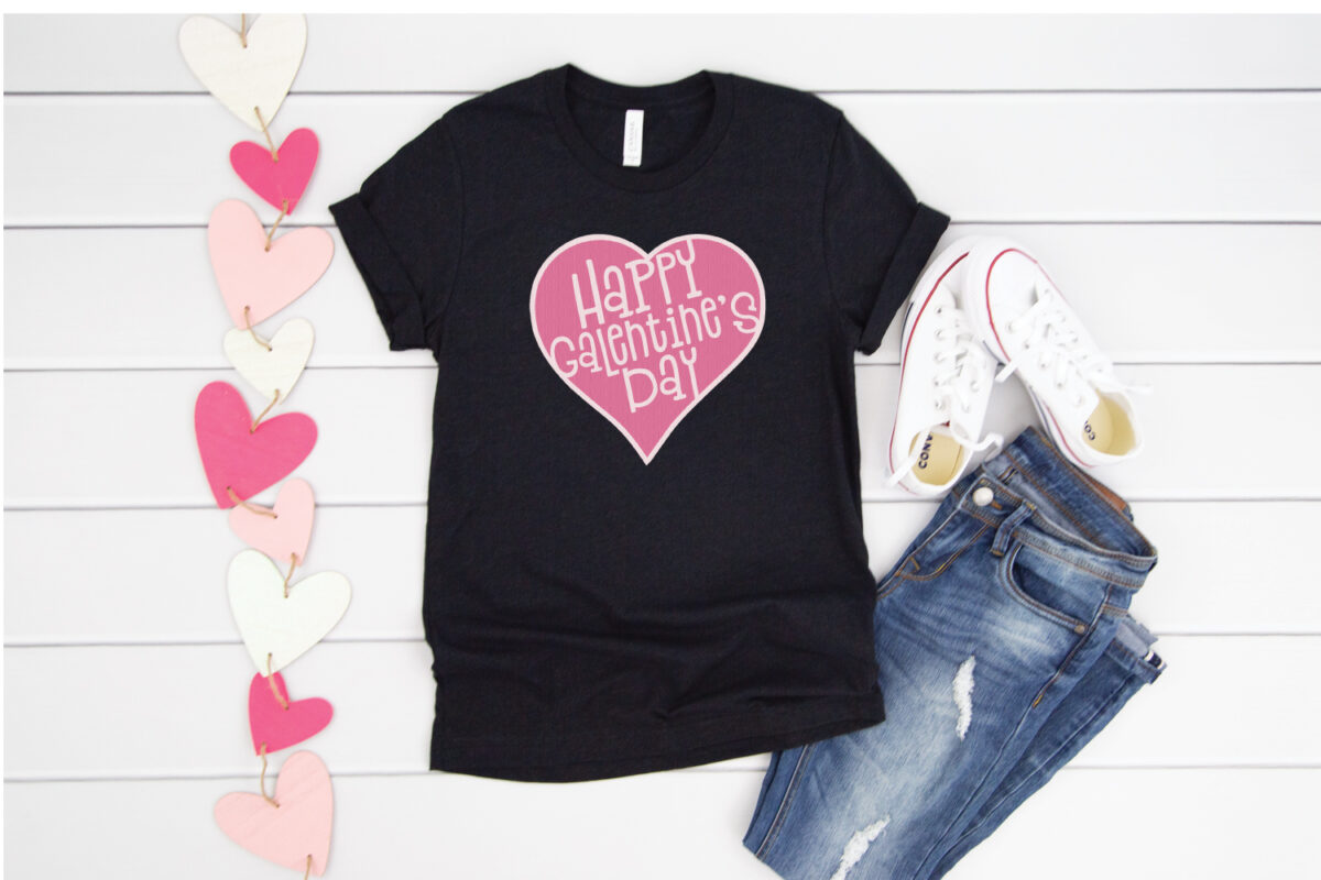 A banner of hearts and a pair of blue jeans and tennis shoes along with a black t-shirt with a pink heart design and the saying, \"Happy Galentine\'s Day\"