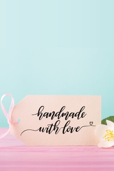 A flower on a pink table lying next to a tag with a pink bow tied to it and the lettering "Handmade with Love" on it
