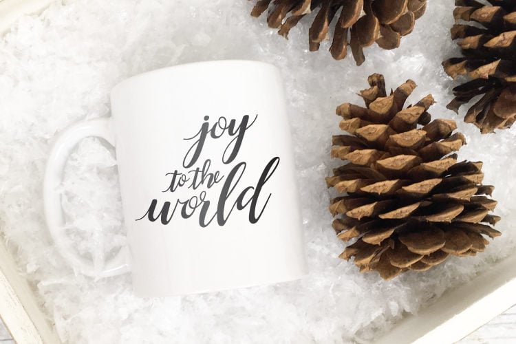 \"Joy to the World\" image on a white mug lying next to pinecones