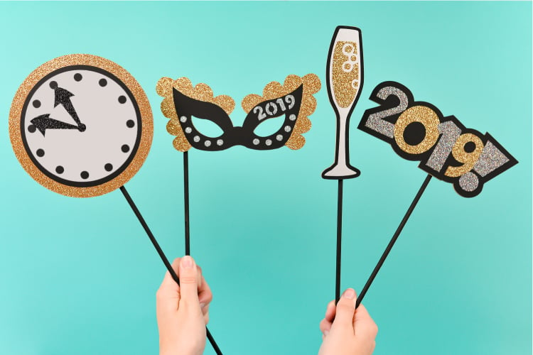 Two hands holding chipboard images of a clock, a mask, a glass of champagne and the year 2019