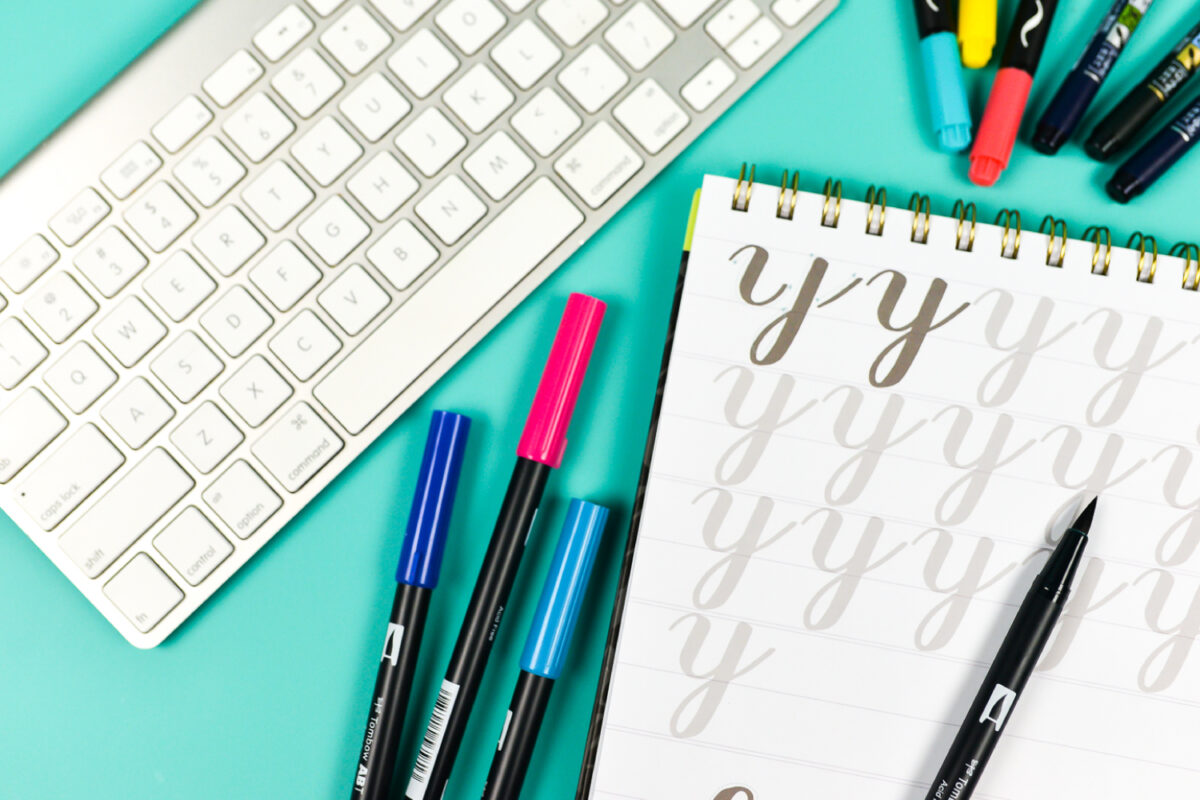 A close up of a keyboard, notebook and several markers