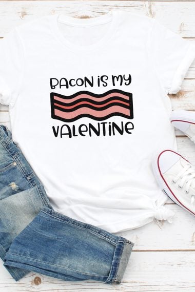 A pair of blue jeans, tennis shoes and a white t-shirt that is designed with a piece of bacon and says, "Bacon is my Valentine"