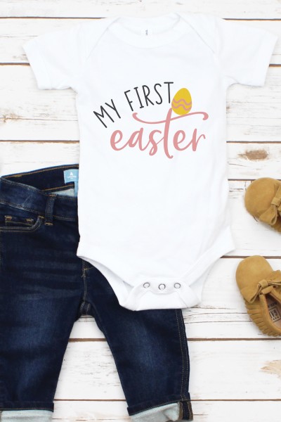 A pair of baby blue jeans, moccasins and a white onesie decorated with an Easter egg and the saying, "My First Easter"