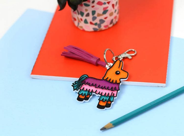 A llama keychain next to a pencil, a tablet of paper and a potted plant