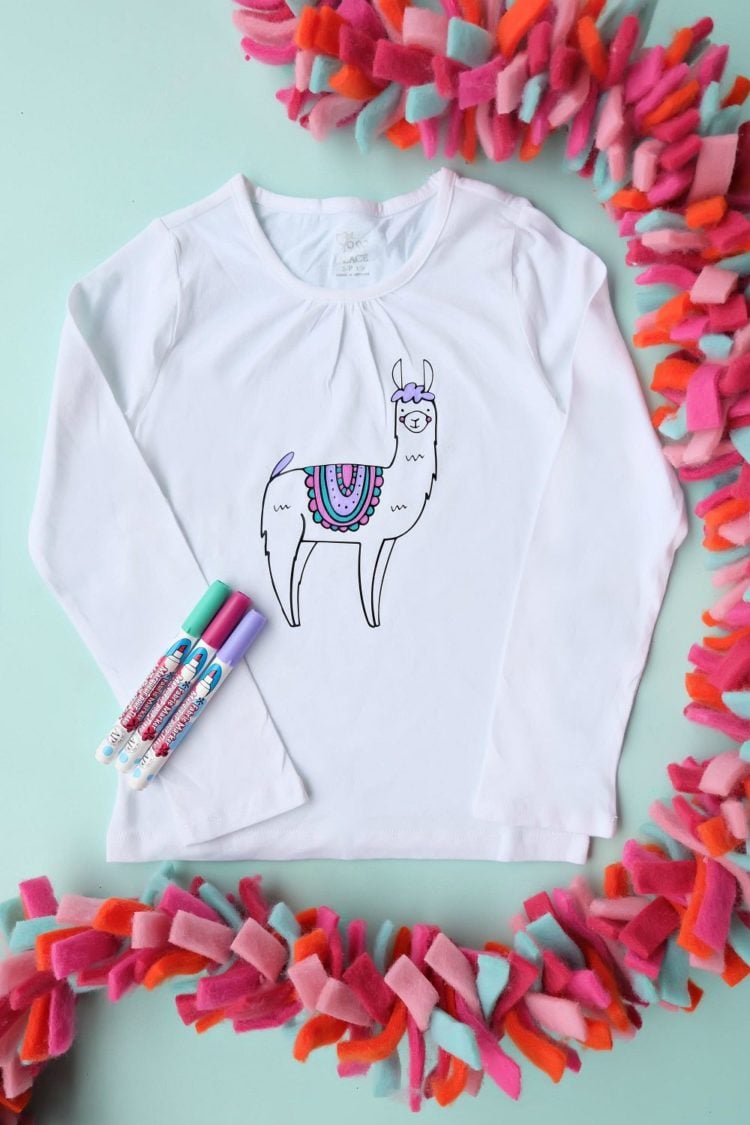 A festive garland and markers by a white long-sleeved shirt with a llama image on it