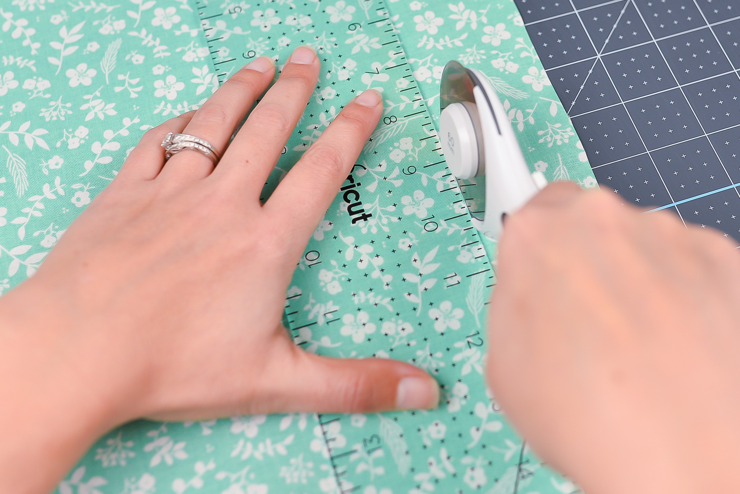 A pair of hands using the Cricut acrylic ruler and the rotary knife cutting a piece of fabric on top of the Crciut self-healing mat