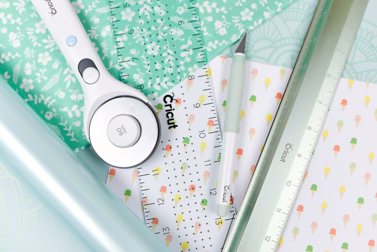 Close up of pieces of fabric and Cricut hand tools of an acrylic ruler, the True Control Knife, a cutting ruler and a rotary cutter