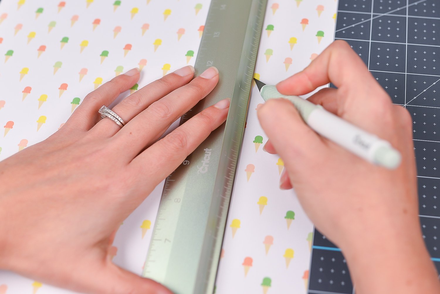 A pair of hands using the Cricut cutting ruler and the True Control knife cutting a piece of fabric on top of the Crciut self-healing mat