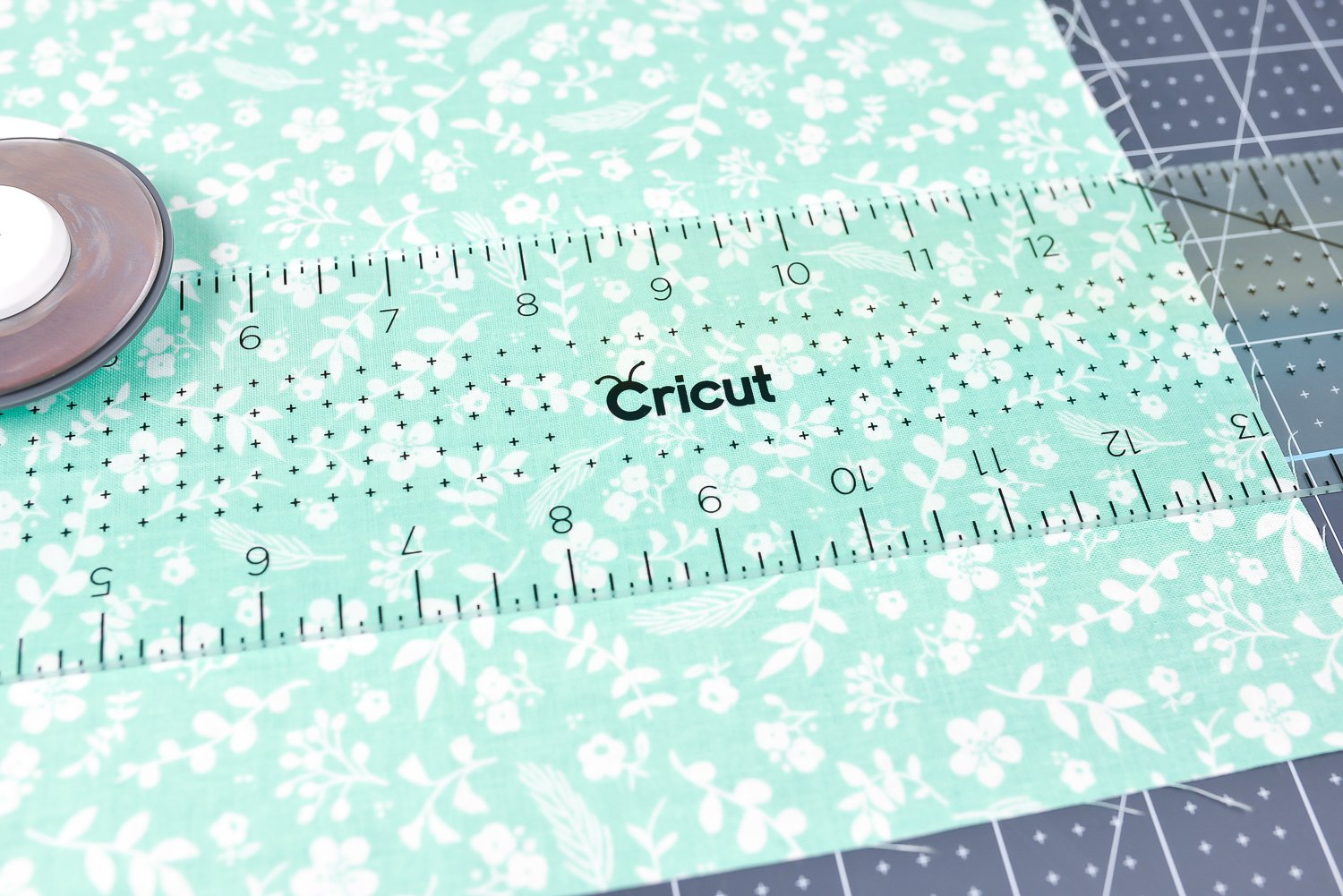Close up of the Cricut acrylic ruler, the rotary cutter and a piece of fabric on top of the Crciut self-healing mat
