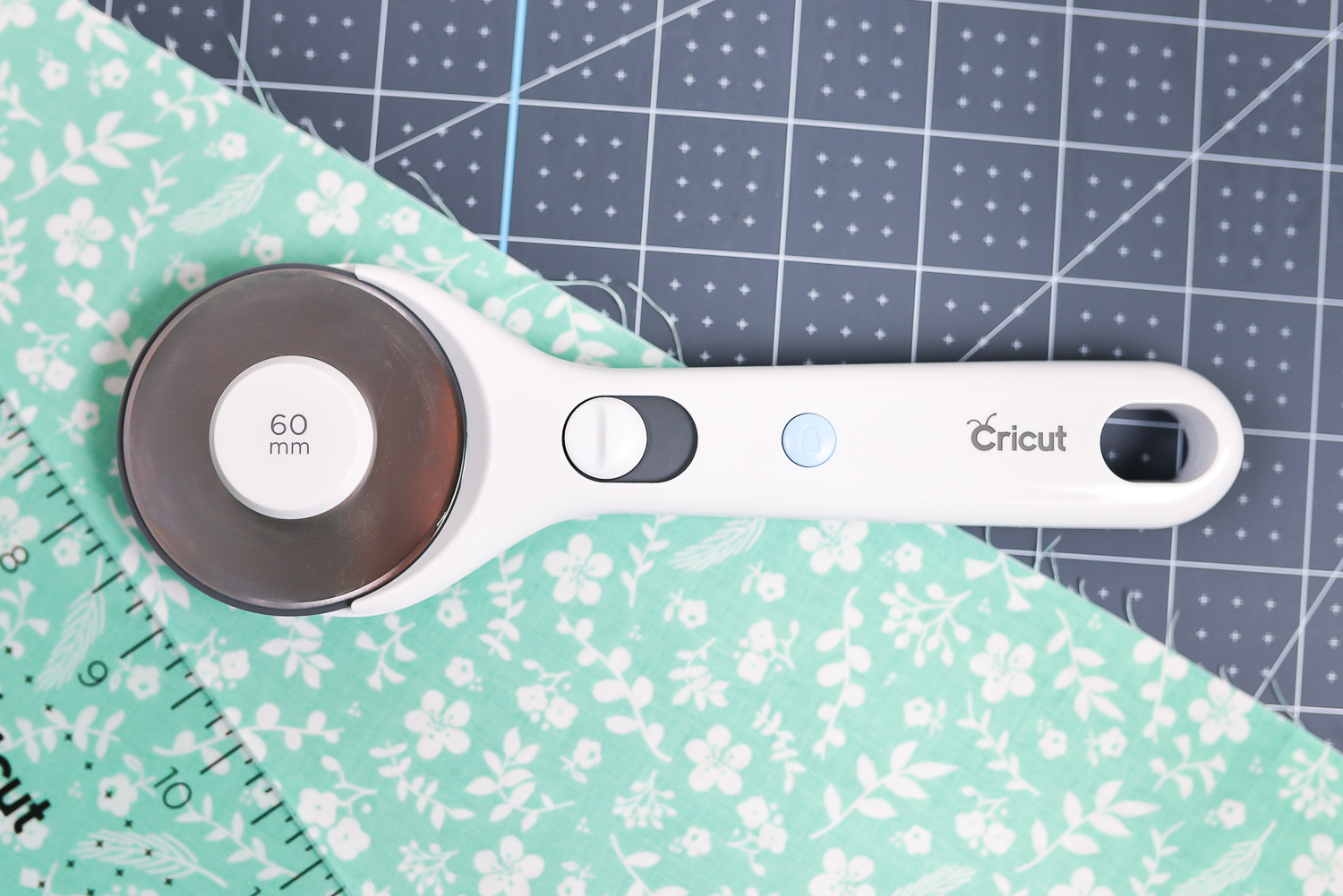 A close up of the Cricut rotary cutter, the acrylic ruler and a piece of fabric on top of the Cricut self-healing mat
