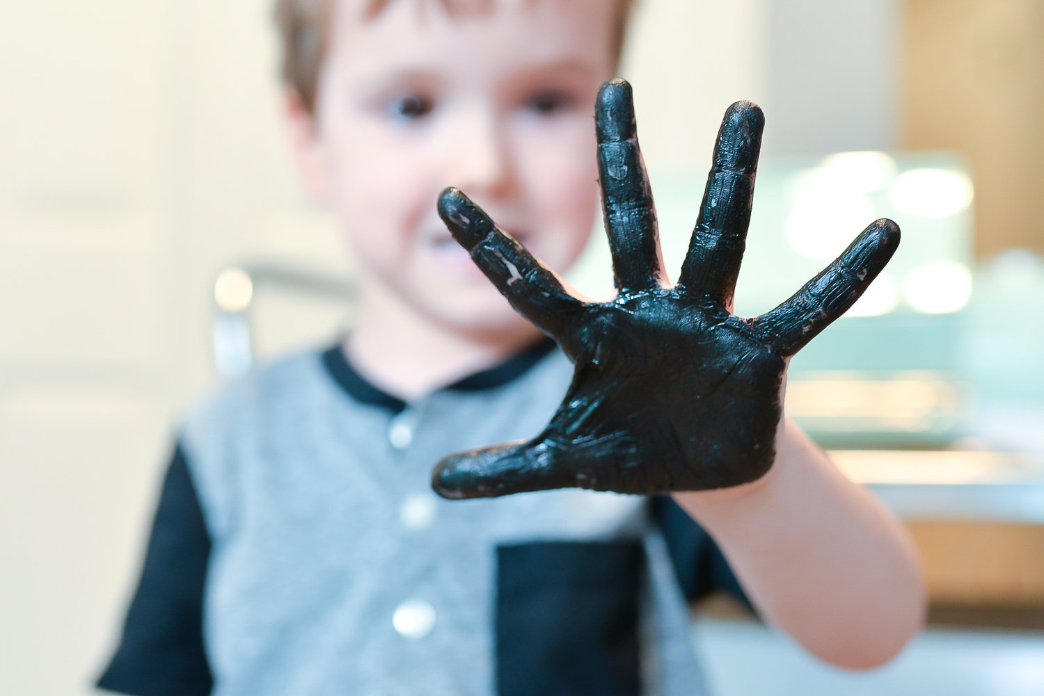 A close up of a little boy holding up his hand that is painted in black paint