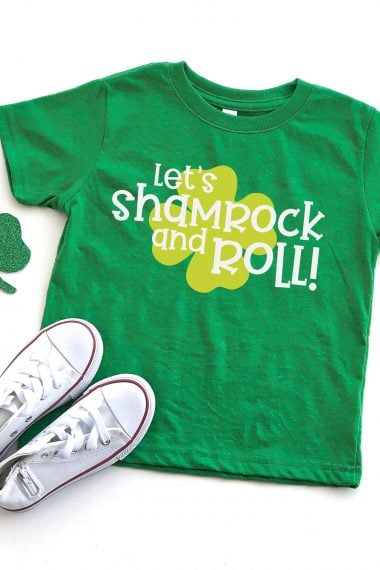 A partial green shamrock with a pair of tennis shoes and a green t-shirt decorated with a light green shamrock with the saying, "Let's Shamrock and Roll!"