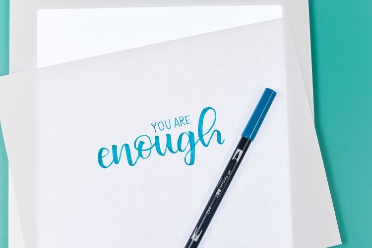 Close up of a Cricut Brightpad with a pen and piece of paper on top of it with the words \'You Are Enough\' written on it