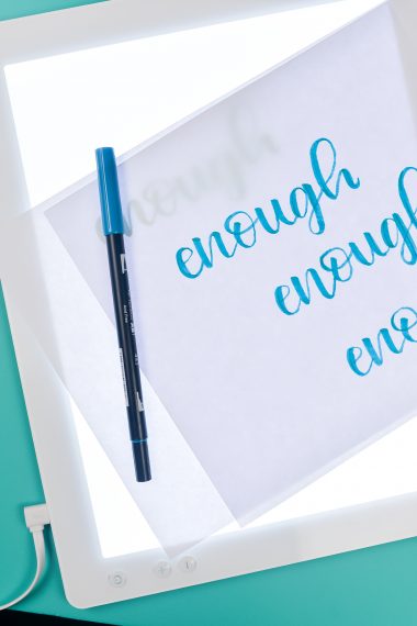 A Cricut Brightpad with a pen and piece of paper on top of it with the word 'enough' written on it