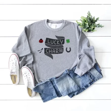 Gray shirt with a ribbon design on it that says Lucky Charm and images of a ladybug, wishbone, shamrock and horseshoe around it