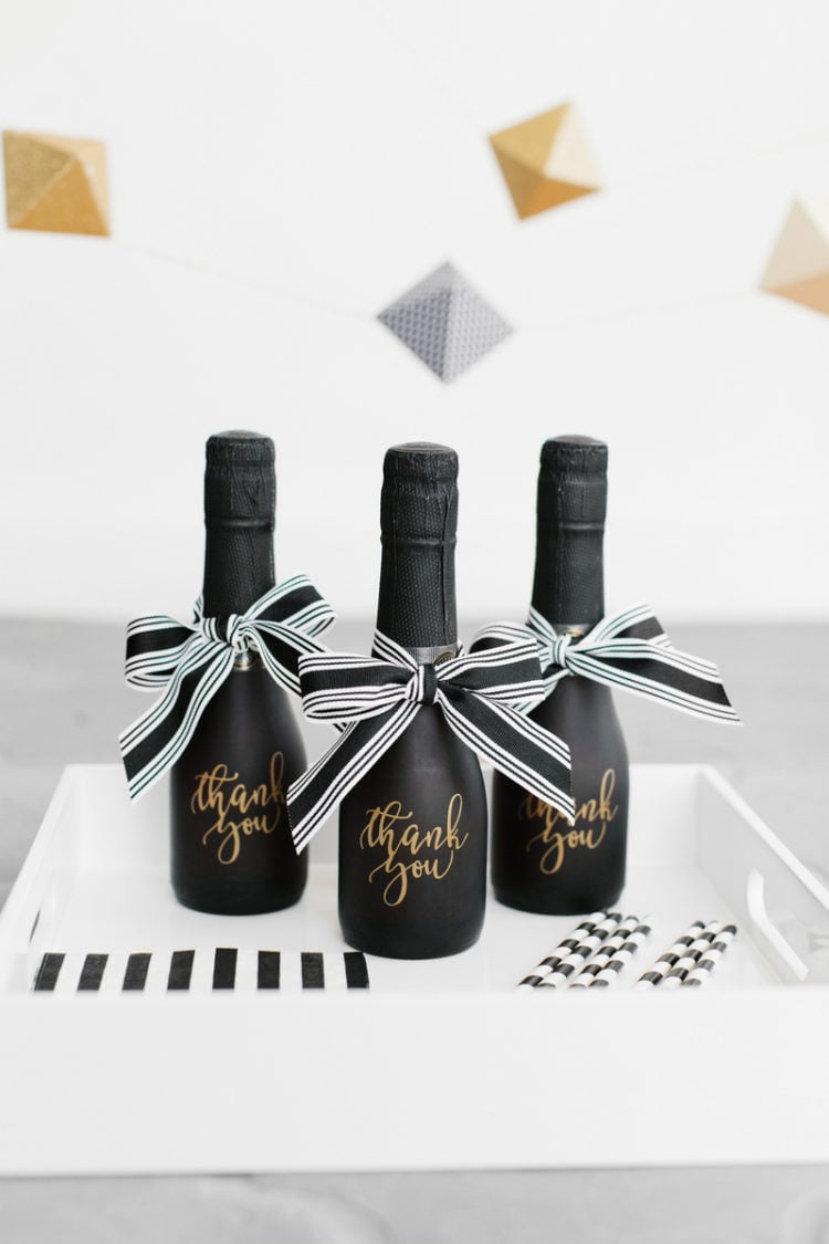A white tray holding three small black bottles of liquid and tied with black and white bows and the words \"Thank You\" on each bottle