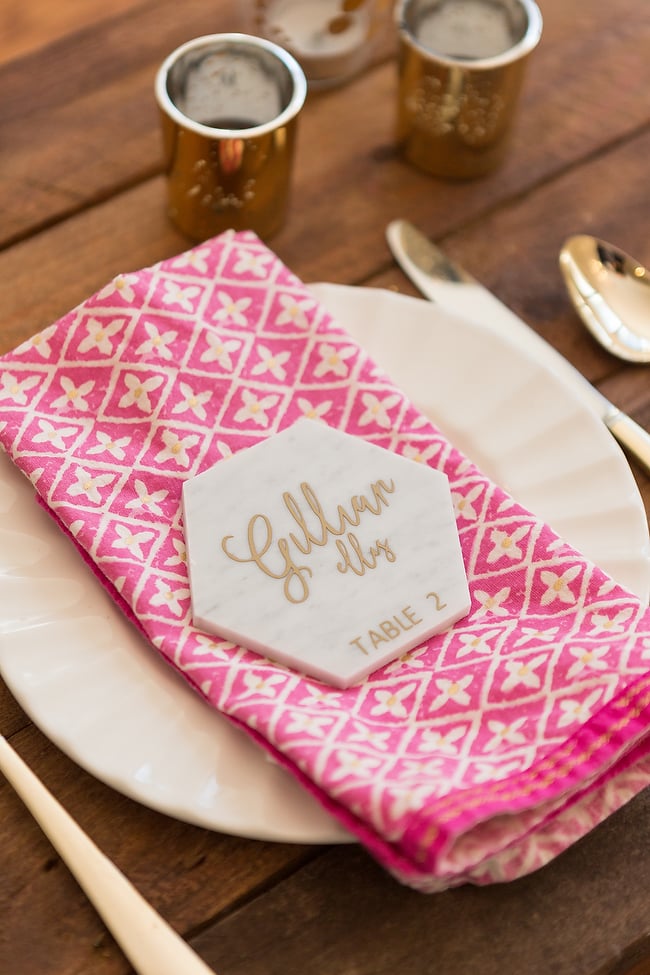 A place setting with a pink and white napkin on top of the plate and on top of the napkin is a marble place card