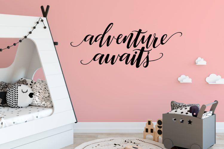 A children\'s bedroom with a pink colored wall with the saying, \"Adventure Awaits\" on it