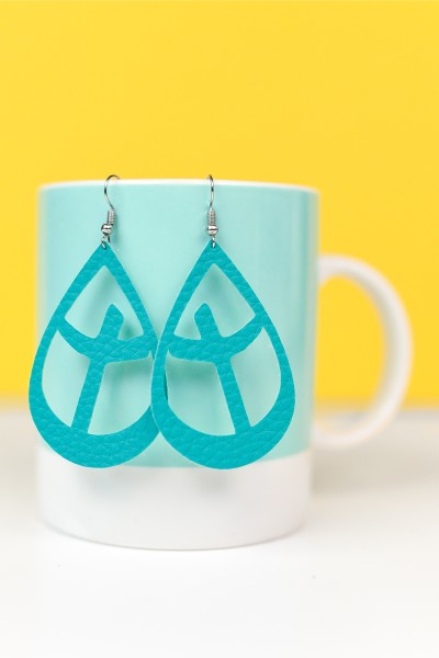 A pair of aqua colored leather earrings hanging from the side of a coffee mug