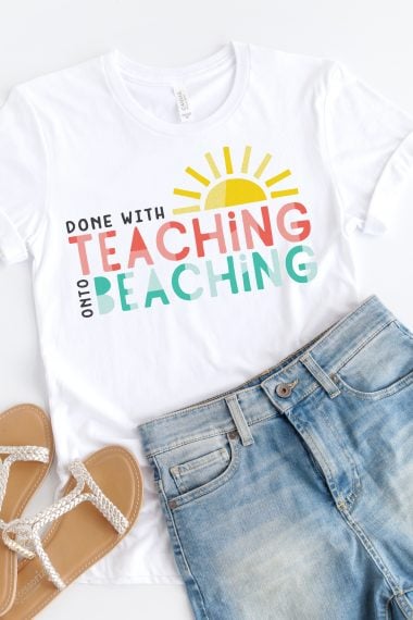 A pair of white sandals, blue jean shorts and a white t-shirt with the design of a half of a sun and the saying, "Done with Teaching onto Beaching"
