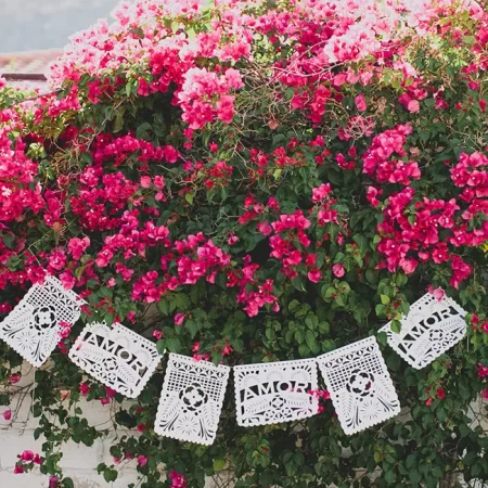 Papel Picado banner hanging from a flowering bush