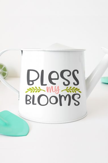 A white watering can with the saying, "Bless My Blooms"