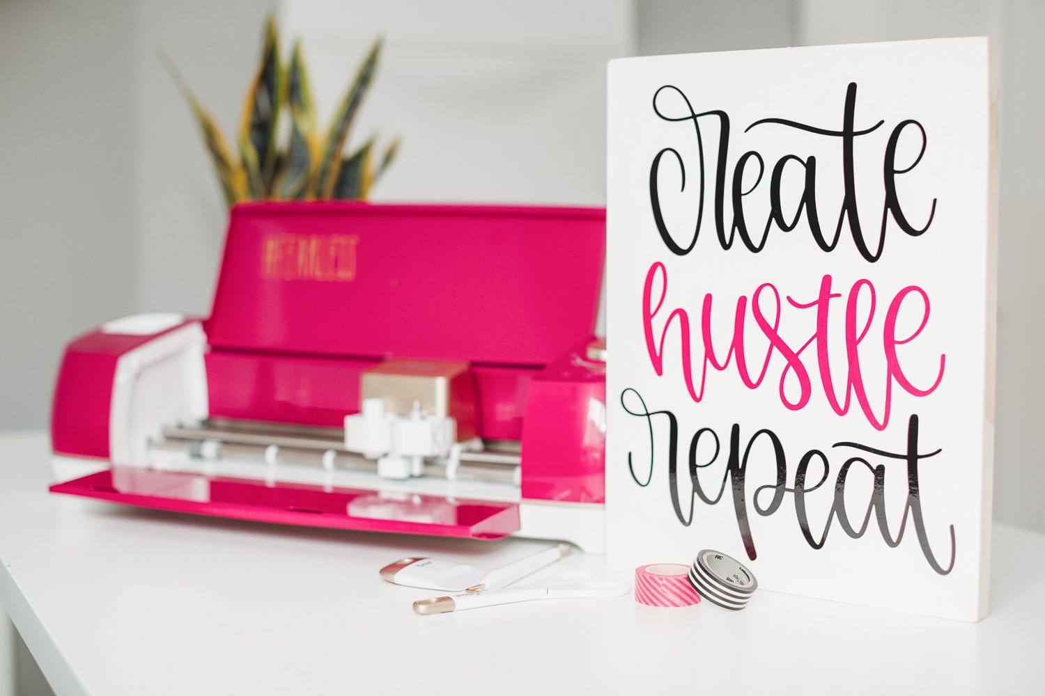 A close up of a red Cricut machine with a sign next to it that says, "Create, Hustle, Repeat"