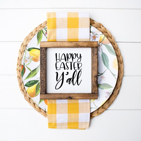 Round woven mat decorated with material and ribbon and a framed square sign that says Happy Easter Y'all