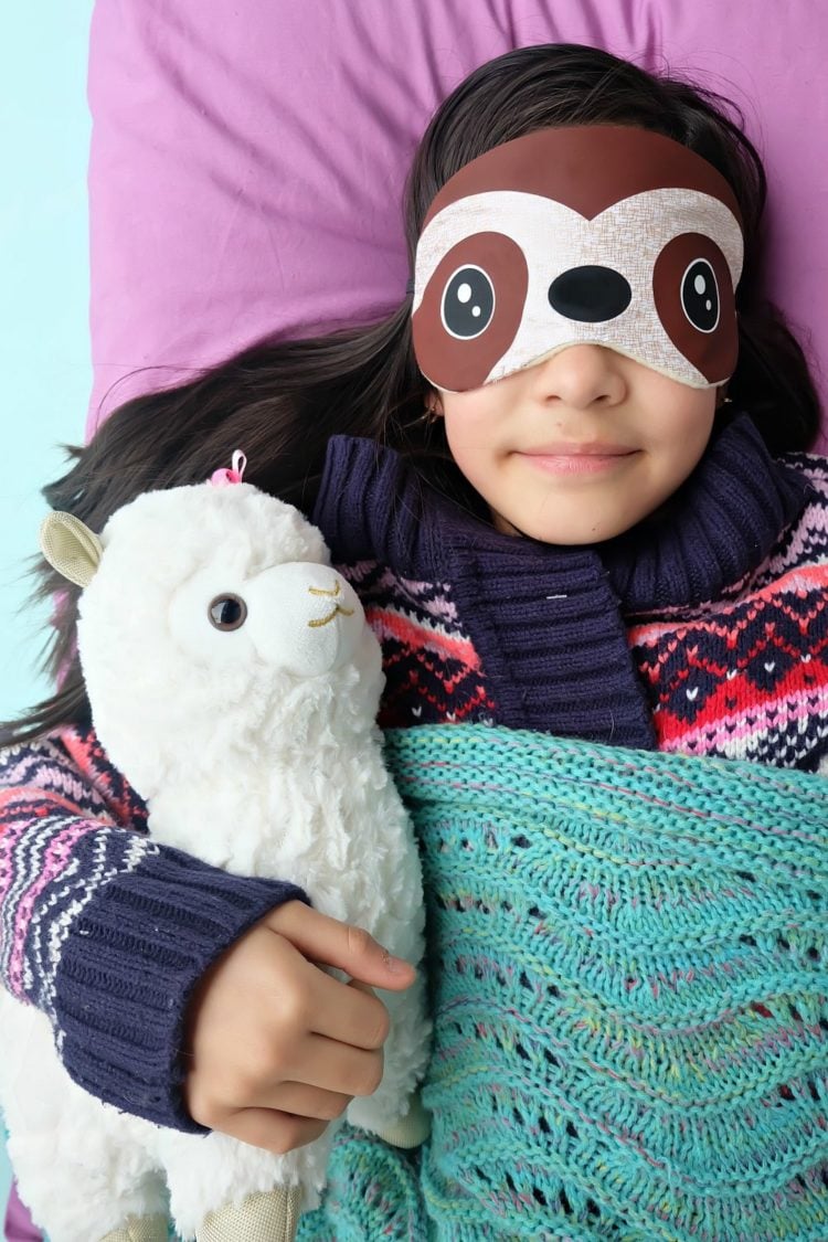 A close up of a person holding a stuffed animal and wearing a sloth sleep mask