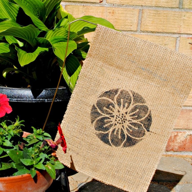 Potted plants around a burlap garden flag that has a flower image on it