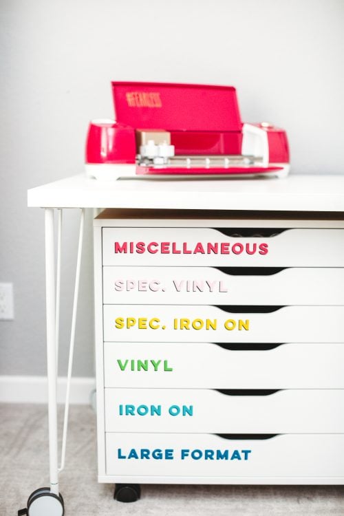 A Cricut machine on top of a table with drawer's underneath that are labeled as "Miscellaneous", "Spec Vinyl", "Spec Iron On", "Vinyl", "Iron On" and "Large Format"